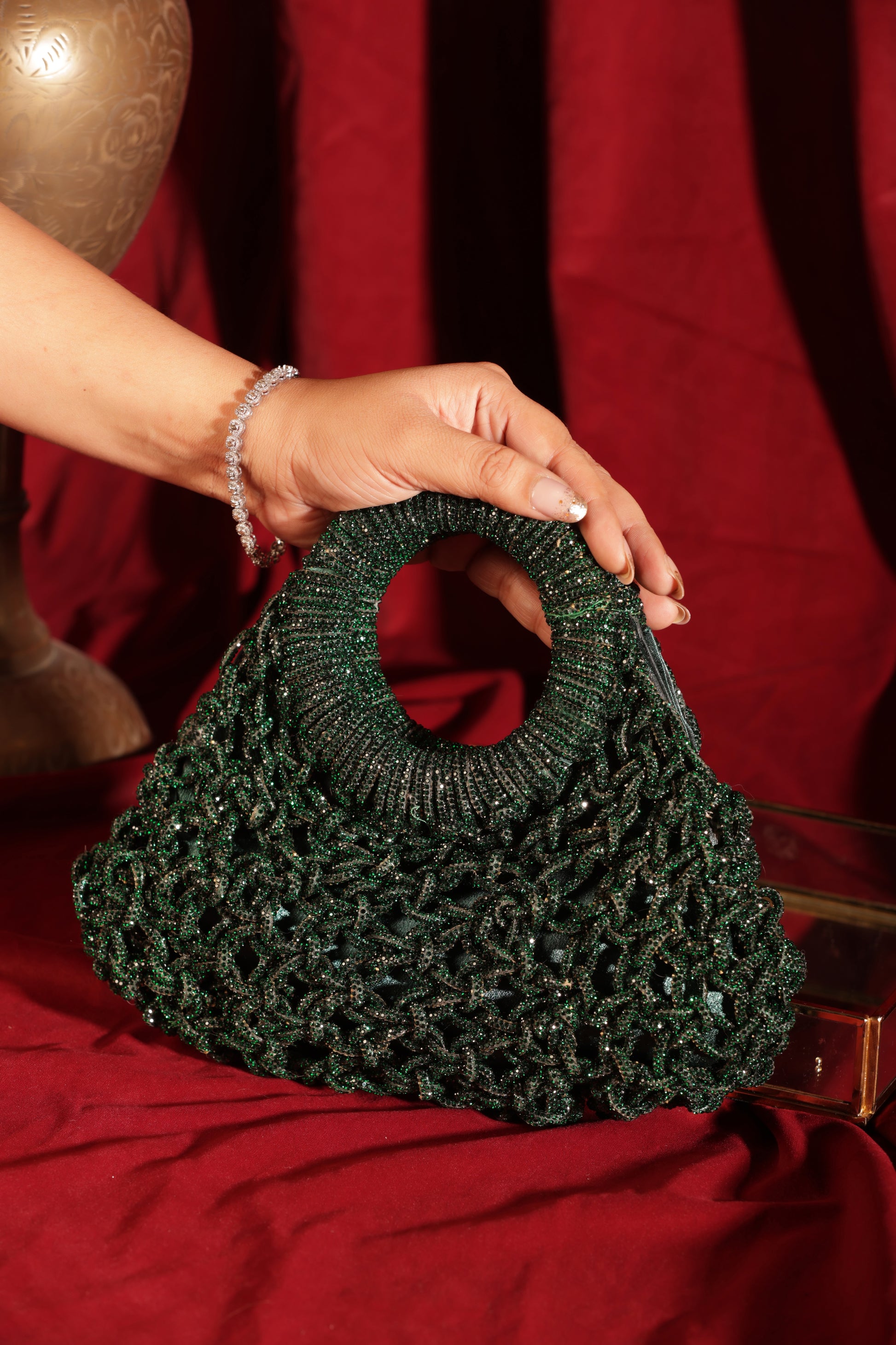 Four shimmering mesh-woven Glimora bags in jewel and metallic tones arranged against rich red fabric.