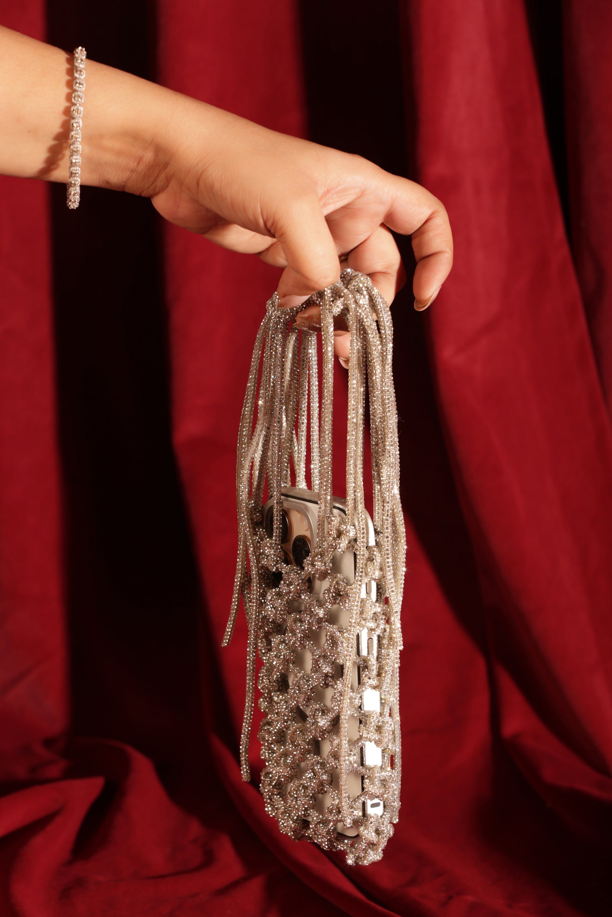 Metallic silver mini sling with long embellished straps, held in hand.