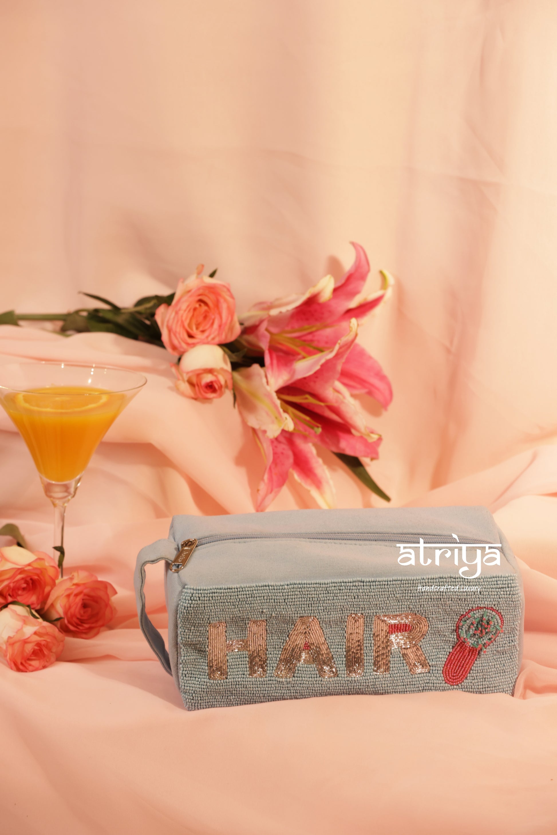 Luxury beaded hair accessories pouch in soft blue with gold lettering, styled with hairbrush and clips in pink feminine editorial setup by Atriya Jaipur.

