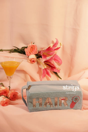 Luxury beaded hair accessories pouch in soft blue with gold lettering, styled with hairbrush and clips in pink feminine editorial setup by Atriya Jaipur.
