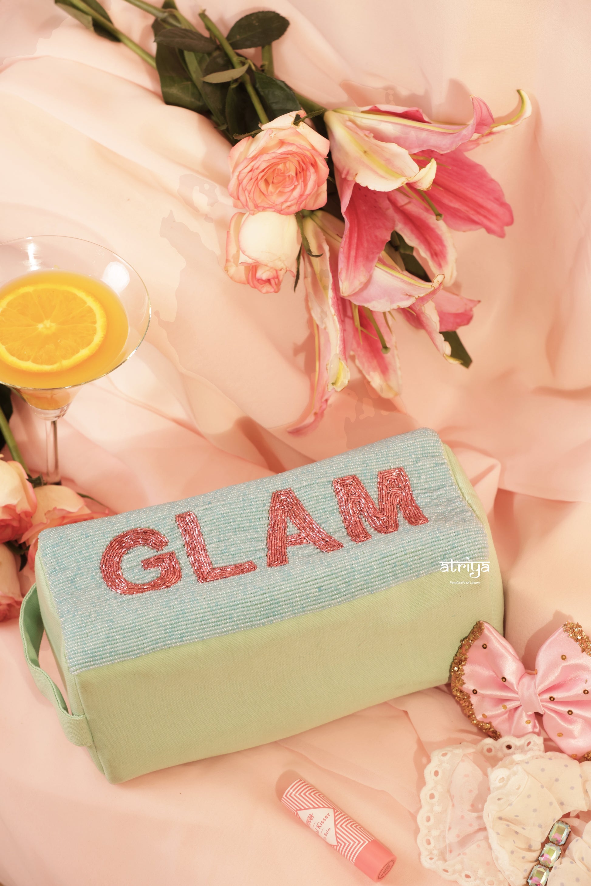 Luxury handcrafted cosmetic pouch in soft mint shade with pink bead detailing, styled with beauty accessories and roses in coquette-inspired editorial setup by Atriya Jaipur.
