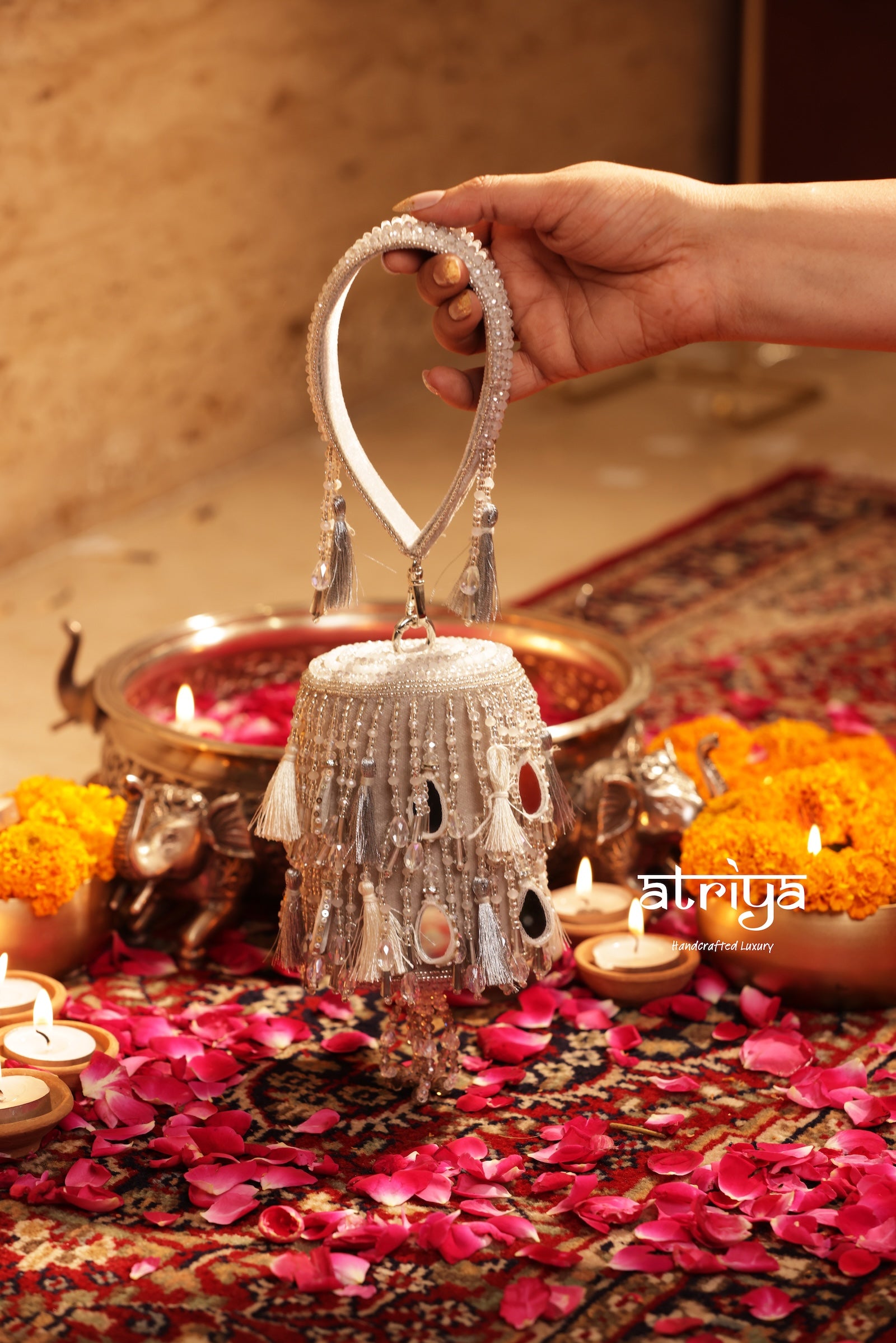 Noorani Silver beaded handbag held by a hand over a festive setup with diya candles and rose petals